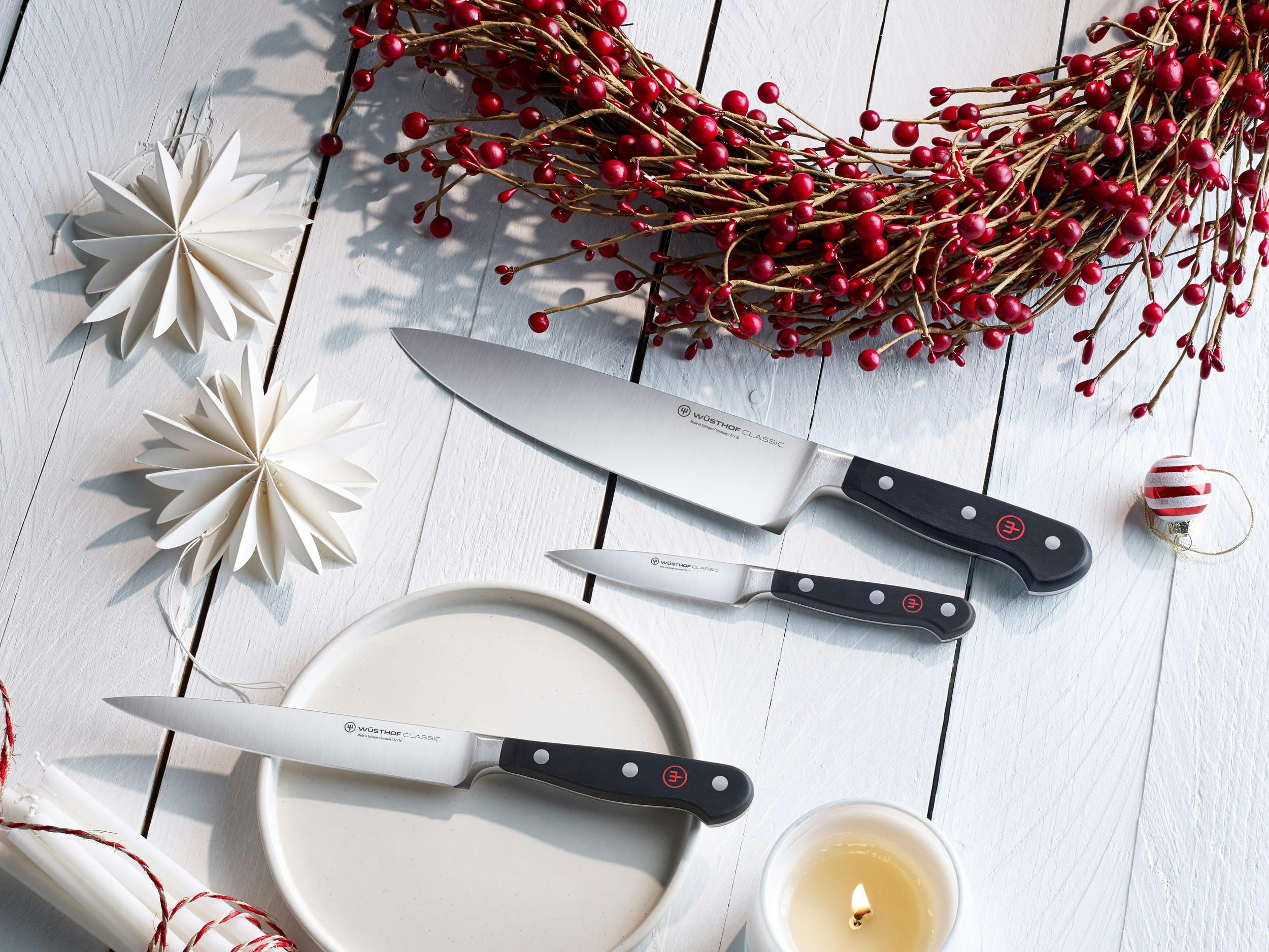 Classic knife set on white wooden table, next to paper snowflakes and holiday wreath